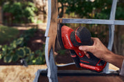 Photo of a hand using CRAFTSMAN CMCW221B cordless detail sander on a wooden furniture piece outdoors.